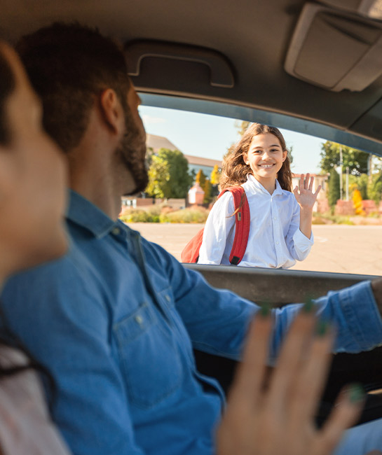 Couple dropping off their daughter at school waving from the car