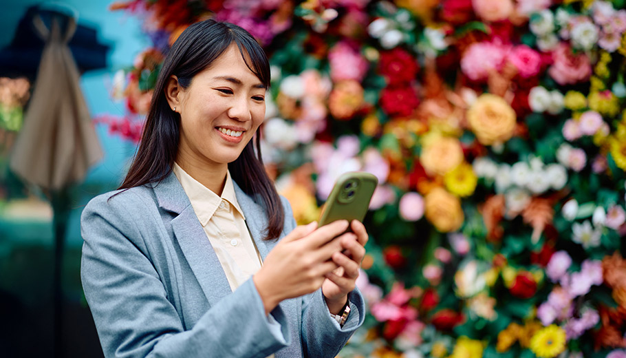 Woman smiling looking at her phone stading outside in front of a flower wall 