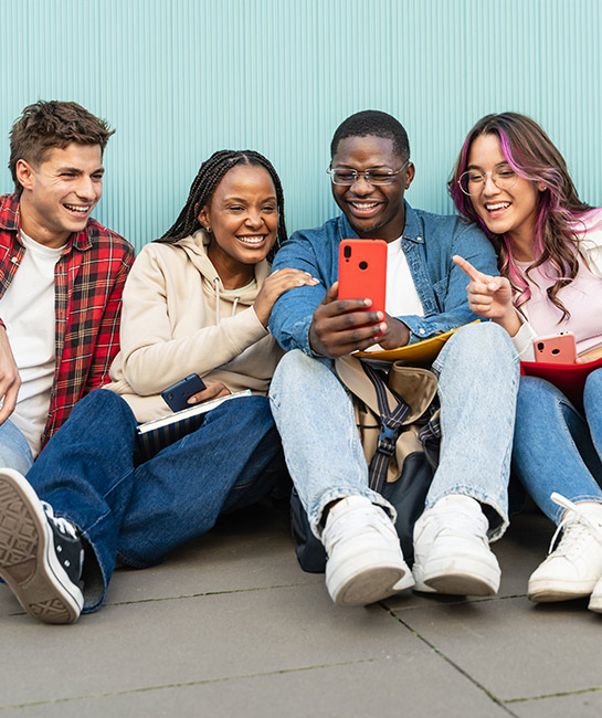 Group of college kids sitting on the ground smiling looking at their phones