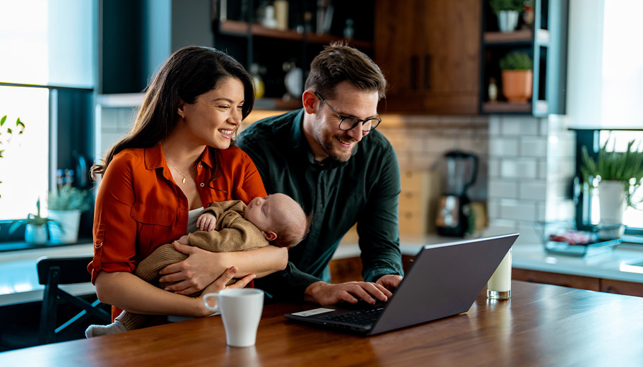 Young couple with a baby looking at a laptop smiling at kitchen island