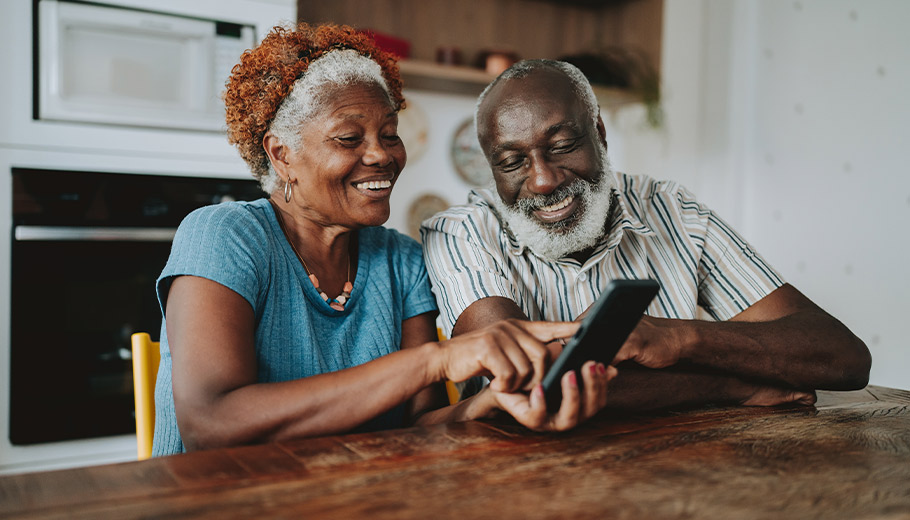 Older couple smiling and looking at a cell phone at their kitchen table
