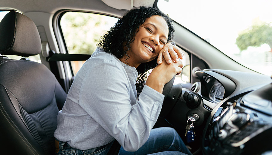 Woman smiling while lying on new car's steering wheel