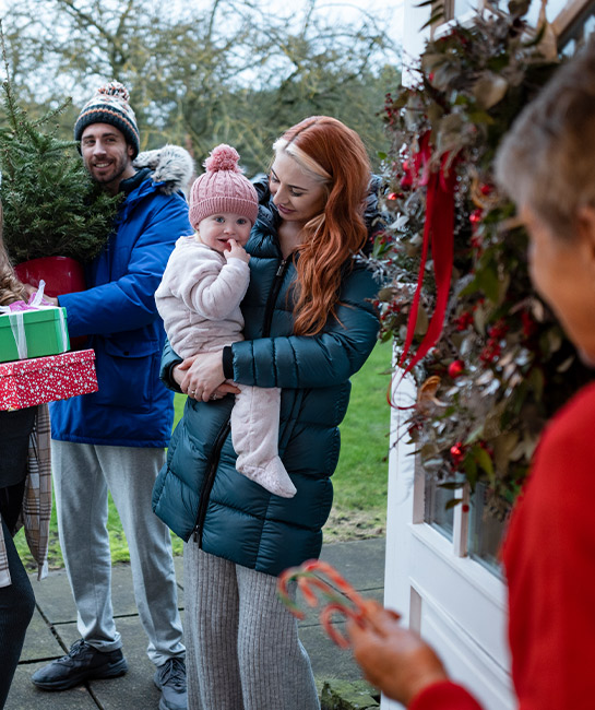 Family visiting other family with gifts in hand at the door
