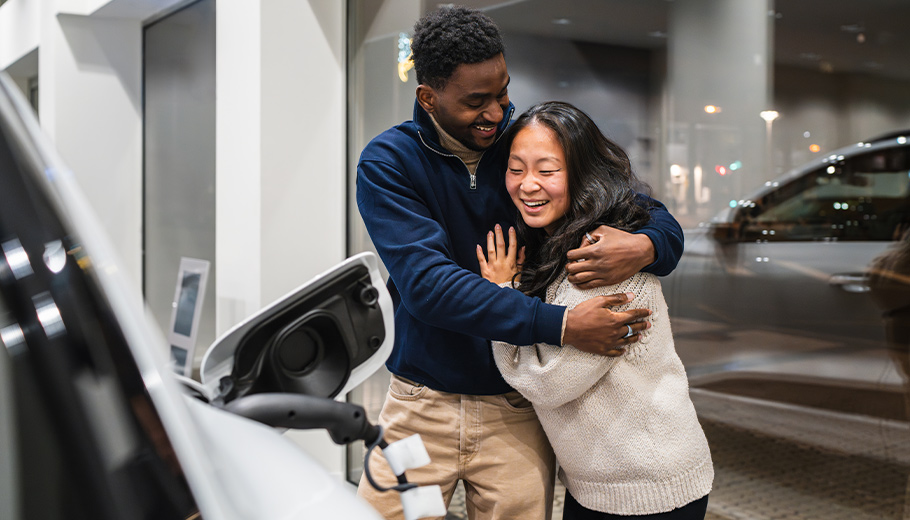 Couple buying a new car at a dealership hugging