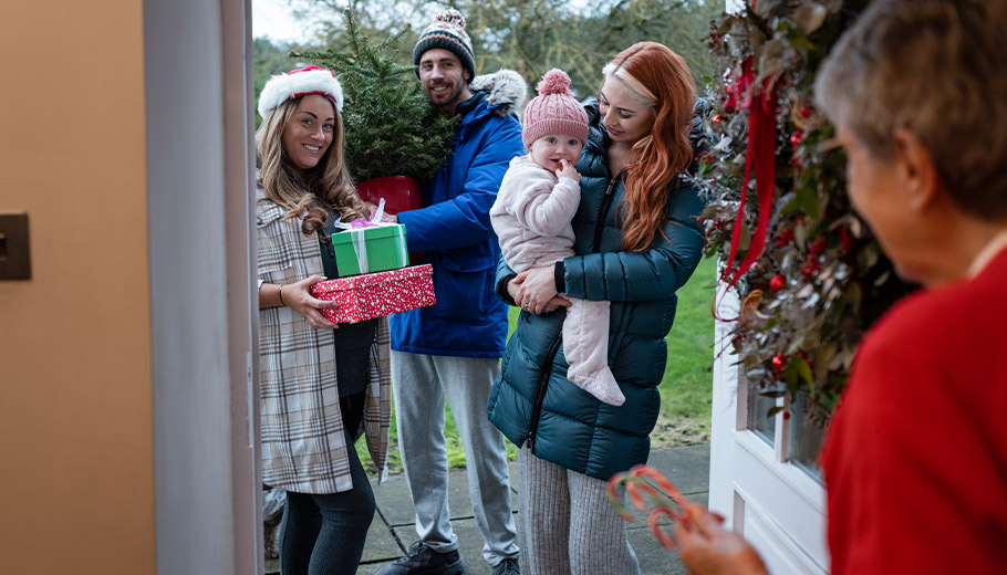 Family visiting other family with gifts in hand at the door