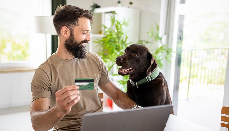 Man and his dog with credit card at a table with a computer. 