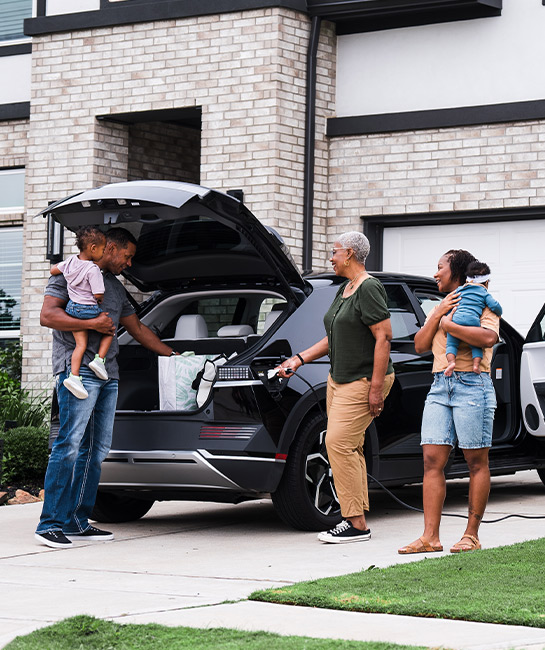 Family with grandmother, parents, and two kids packing trunk of their electric vehicle