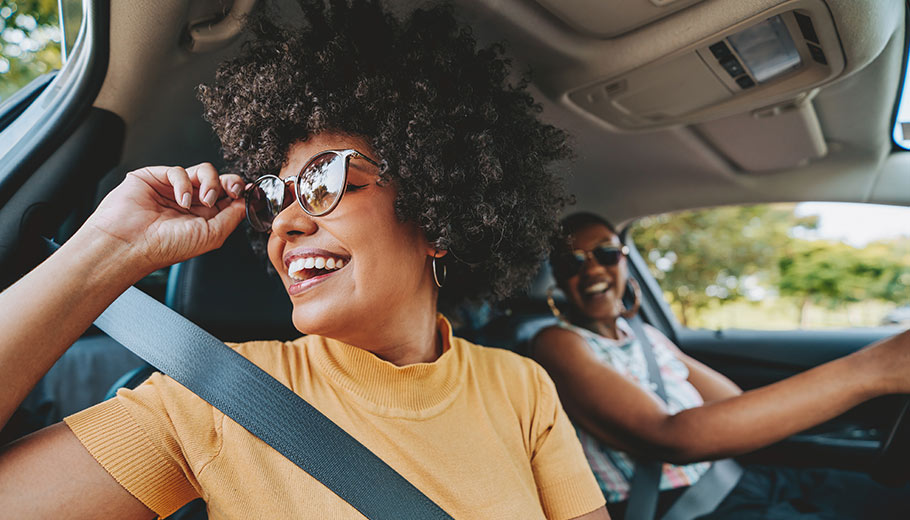 Two women friends driving and smiling with sunglasses on