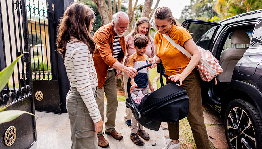 Older couple welcoming their family outside their home by a car