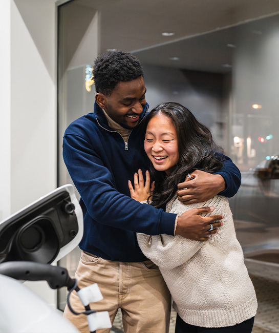 Couple buying a new car at a dealership hugging