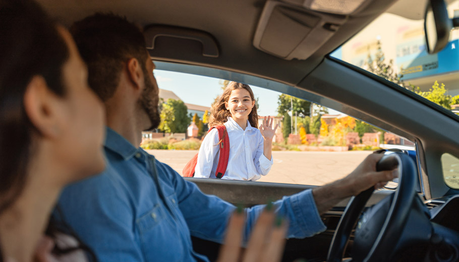 Couple dropping off their daughter at school waving from the car
