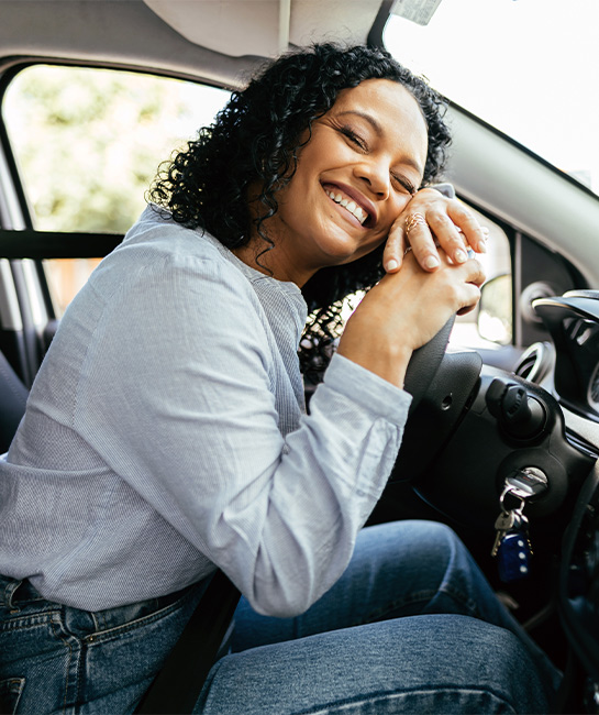 Woman smiling while lying on new car's steering wheel