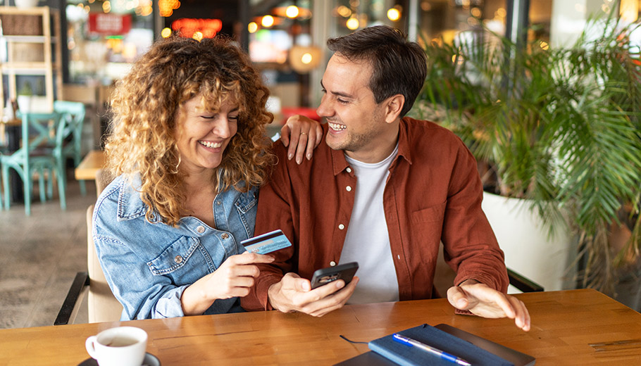 Couple at table looking at their cell phone smiling and holding a credit card