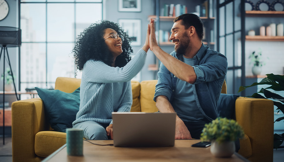 Couple high fiving on their couch with laptop on table in front of them