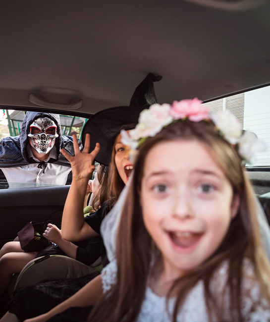 young kids pretending to be scared in the back of a car wearing Halloween costumes
