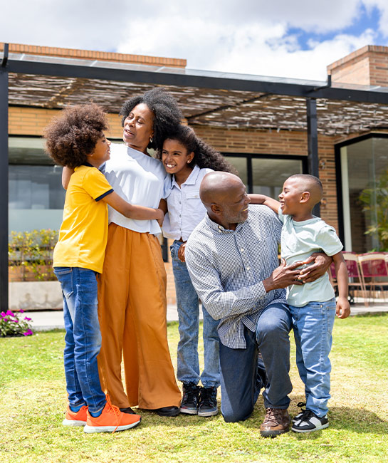 Family of five standing outside their new home on a sunny day smiling 