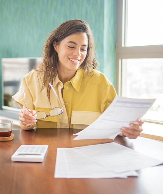 woman smiling while looking at paperwork with her laptop on table