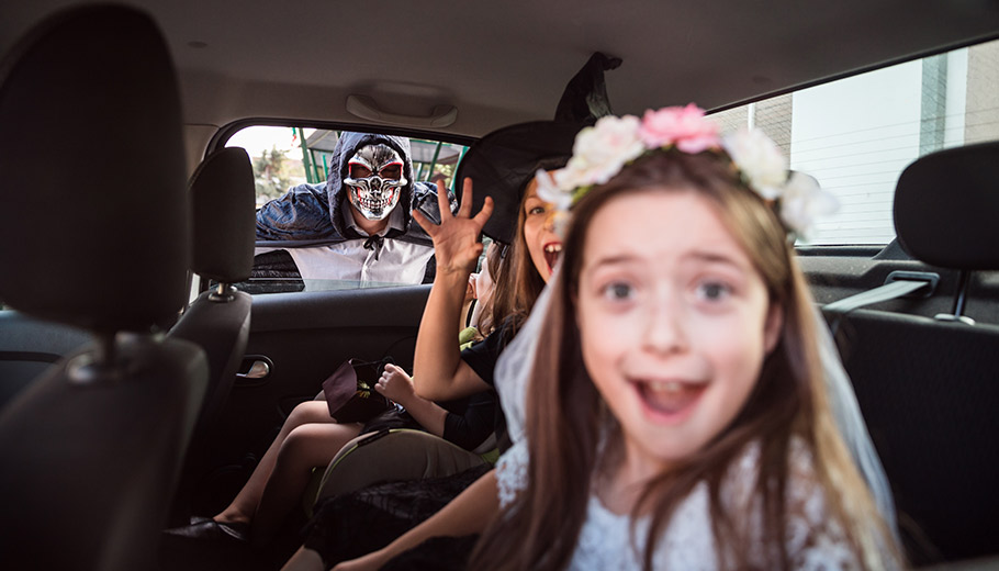 young kids pretending to be scared in the back of a car wearing Halloween costumes