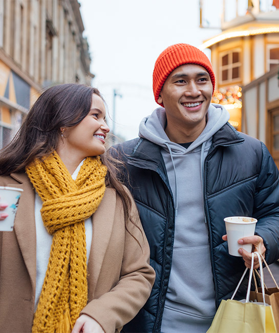Couple holiday shopping outdoors holding coffee and bags smiling
