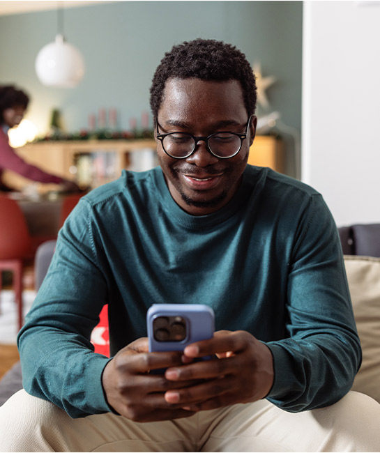 Man looking at his phone smiling with woman in background out of focus