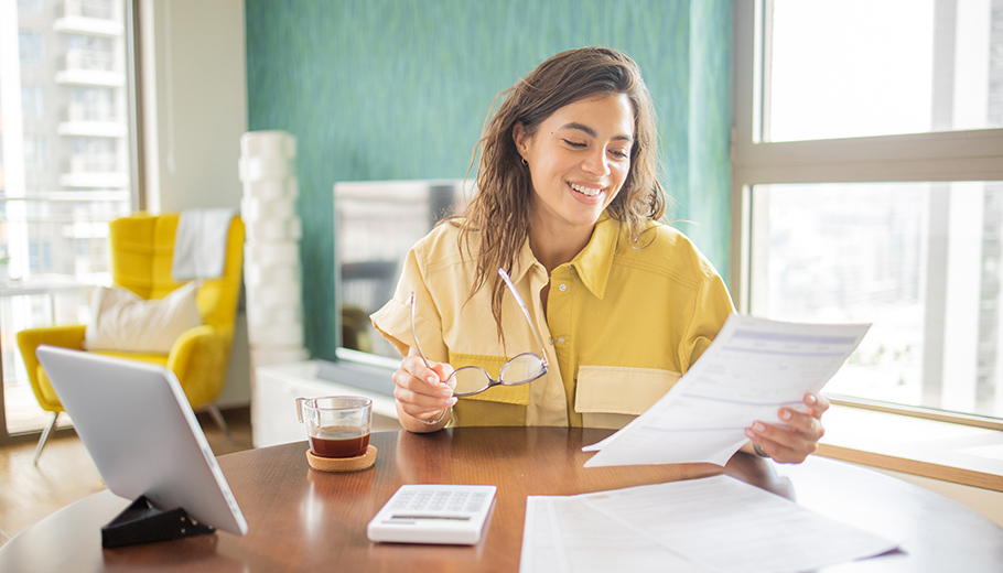 woman smiling while looking at paperwork with her laptop on table